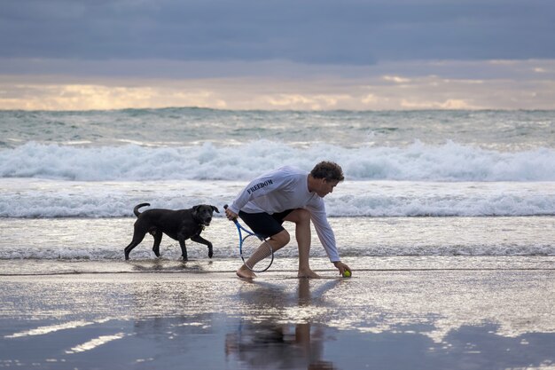 Uomo con cane nero sulla spiaggia di Piha