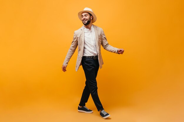 Uomo con cappello e vestito elegante che si muove su sfondo arancione