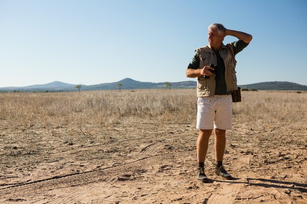 Uomo con distogliere lo sguardo binoculare mentre levandosi in piedi sul paesaggio