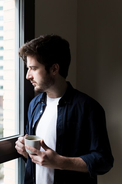 Uomo con drink guardando fuori la finestra dell&#39;ufficio