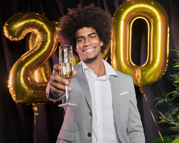 Uomo con felice anno nuovo 2020 palloncini e bicchiere di champagne