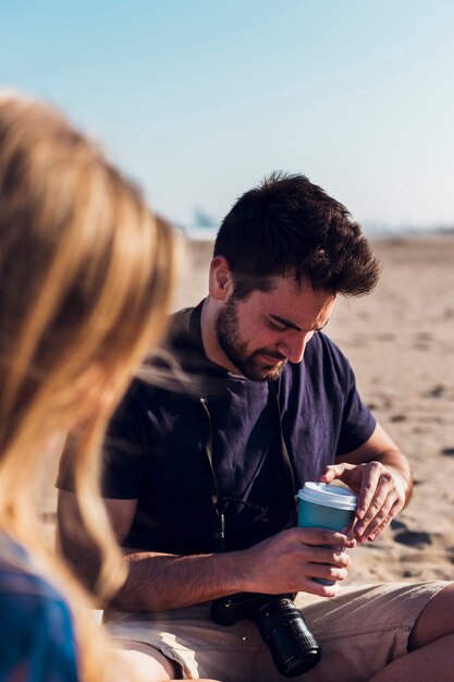 Uomo con fotocamera e tazza sulla spiaggia