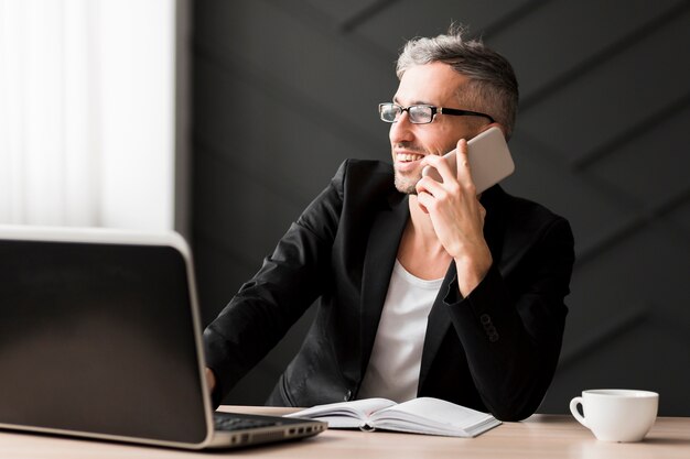 Uomo con giacca nera, guardando lontano e tenendo il telefono cellulare