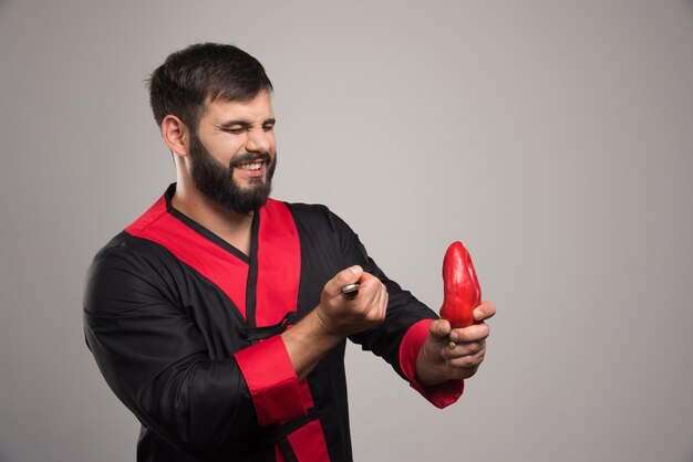 Uomo con gli occhi chiusi che tiene un peperone rosso sul muro grigio