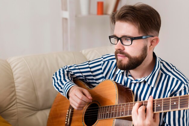 Uomo con gli occhiali a suonare la chitarra a casa