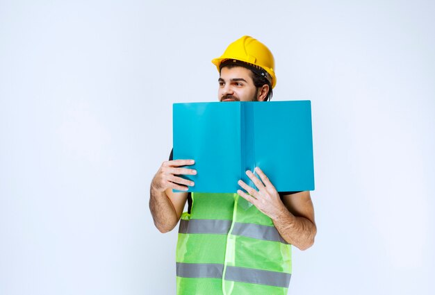 Uomo con il casco che tiene una cartella blu sul viso.