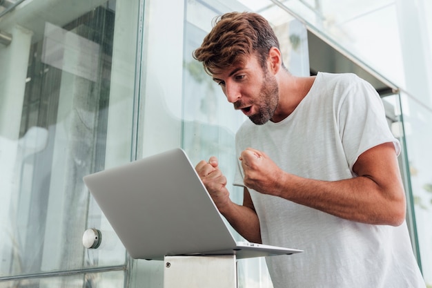 Uomo con il computer portatile che celebra con i pugni