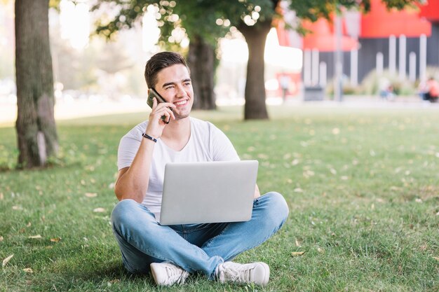 Uomo con il computer portatile che parla sul cellulare in giardino