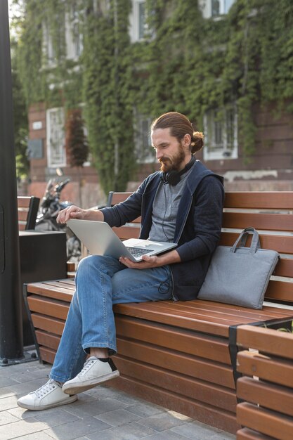 Uomo con il computer portatile e le cuffie all'aperto nella città