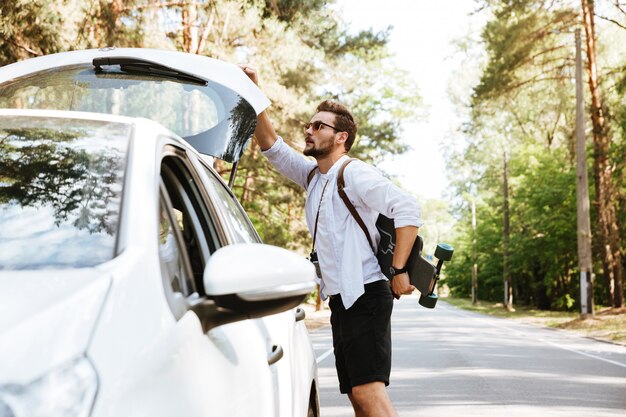 Uomo con il pattino all'aperto che sta automobile vicina