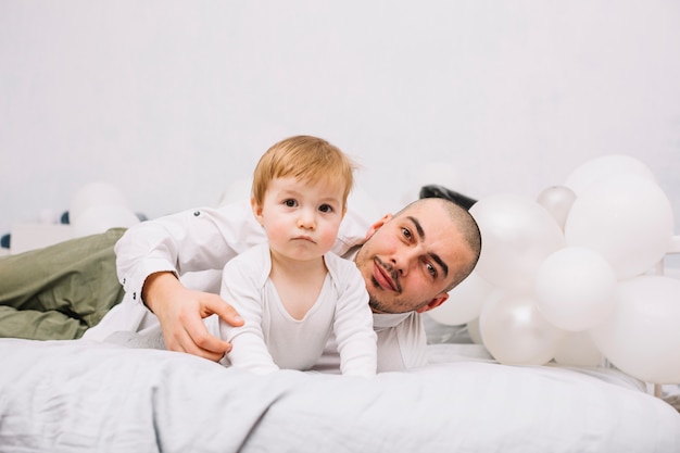 Uomo con il piccolo bambino sul letto vicino a palloncini