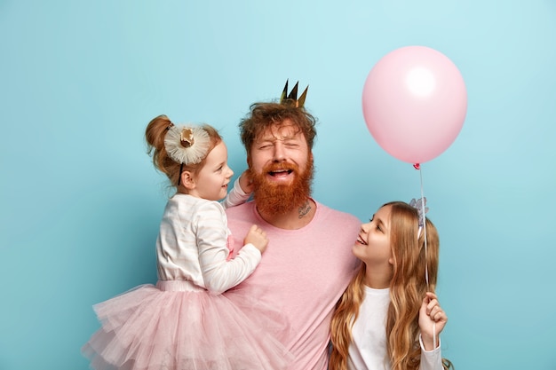 Uomo con la barba allo zenzero e le sue figlie con accessori da festa