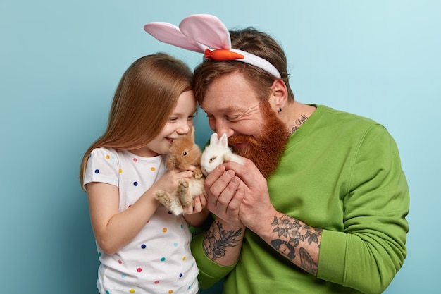 Uomo con la barba allo zenzero indossando abiti colorati e sua figlia che tiene il coniglio