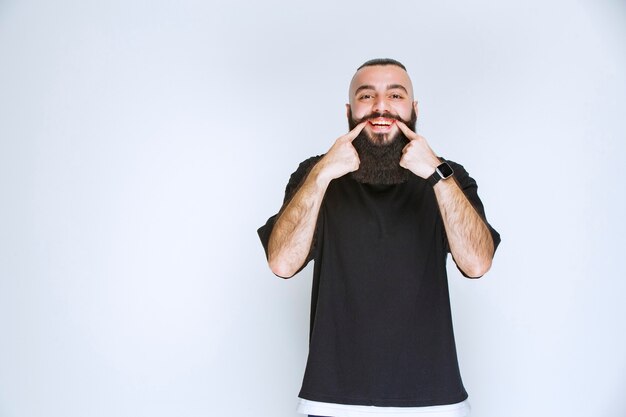 Uomo con la barba che indica il suo sorriso.