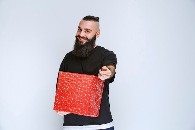 Uomo con la barba che offre una confezione regalo rossa