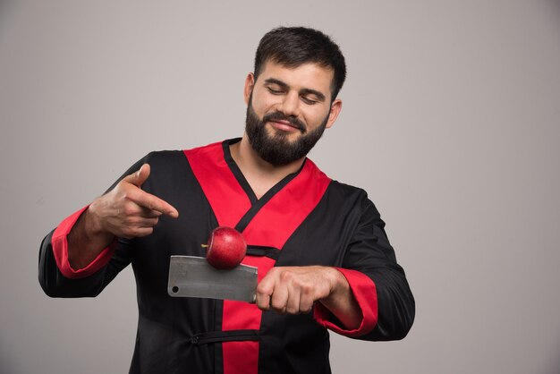 Uomo con la barba che punta alla mela rossa sul coltello.