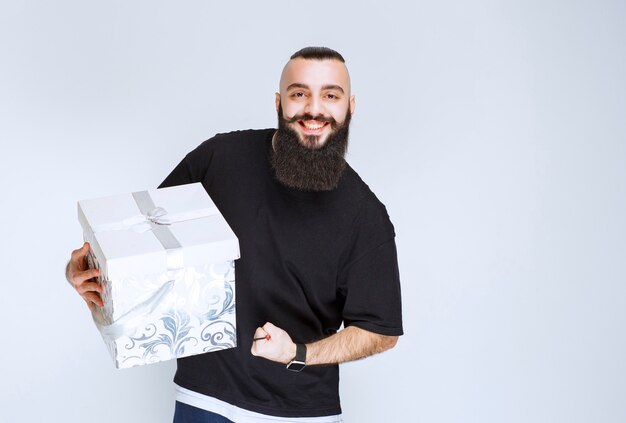 Uomo con la barba che tiene in mano una confezione regalo blu bianca e si sente di successo.