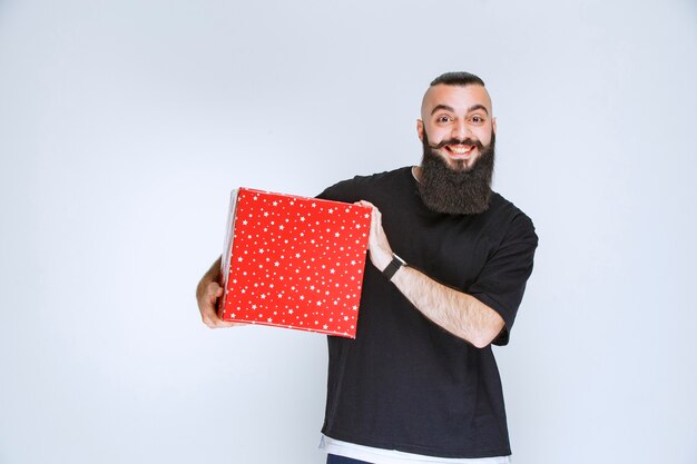 Uomo con la barba che tiene la sua confezione regalo rossa, si diverte e si sente felice.