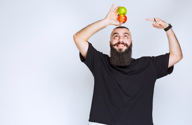 Uomo con la barba che tiene le mele sopra la sua testa.