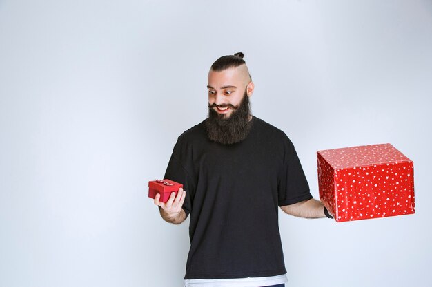 Uomo con la barba che tiene scatole regalo rosse con entrambe le mani e prende una decisione.