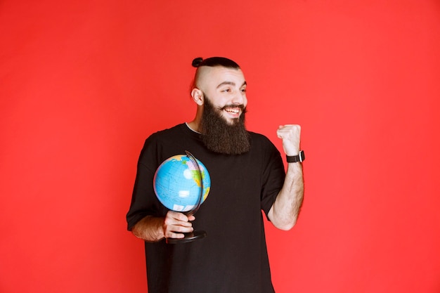 Uomo con la barba che tiene un globo e mostra il pugno.