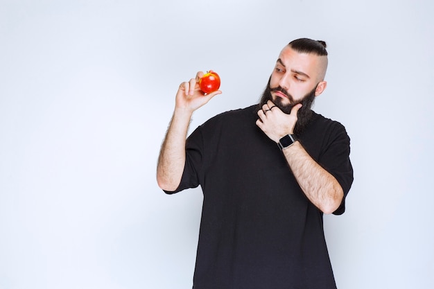 Uomo con la barba che tiene una mela rossa o una pesca e pensa.