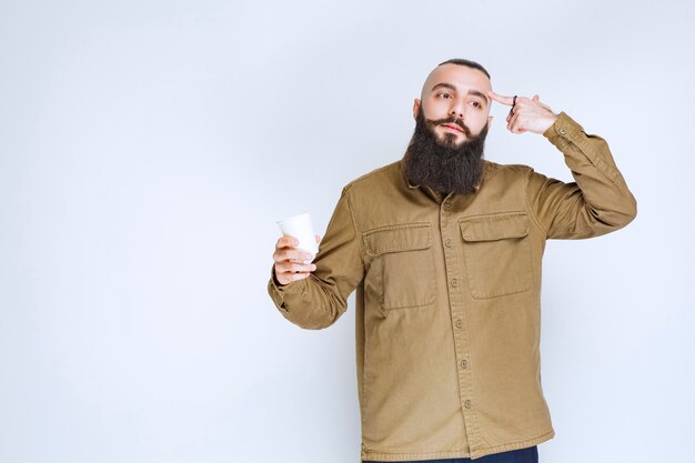 Uomo con la barba che tiene una tazza di caffè e pensa.