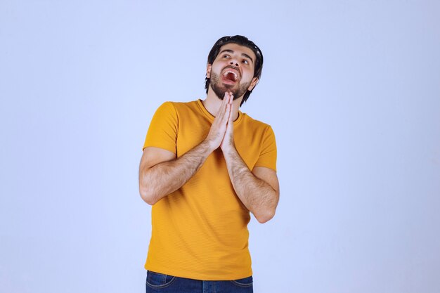 Uomo con la barba che unisce le mani e prega e chiede qualcosa