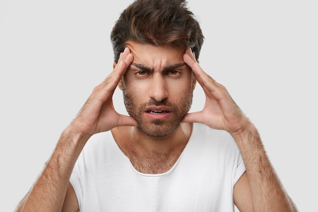 Uomo con la barba lunga esasparato tiene le mani sulle tempie, ha un terribile mal di testa, si sente stanco del lavoro costante, ha la barba scura