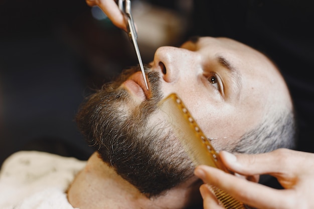 Uomo con la barba. Parrucchiere con un cliente. Uomo con un pettine e delle forbici