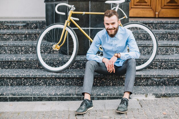 Uomo con la bicicletta che si siede sulla costruzione di scale