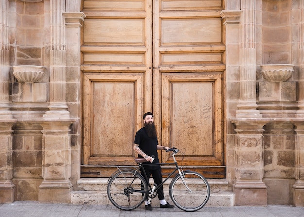 Uomo con la bicicletta che sta davanti alla grande parete di legno d&#39;annata chiusa