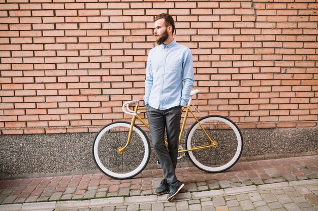 Uomo con la bicicletta vicino al muro di mattoni