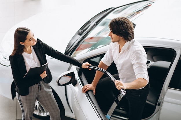 Uomo con la donna in una sala d'esposizione dell'automobile che sceglie un'automobile