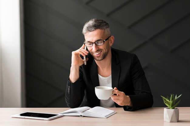 Uomo con la giacca nera che parla su un telefono e che beve caffè