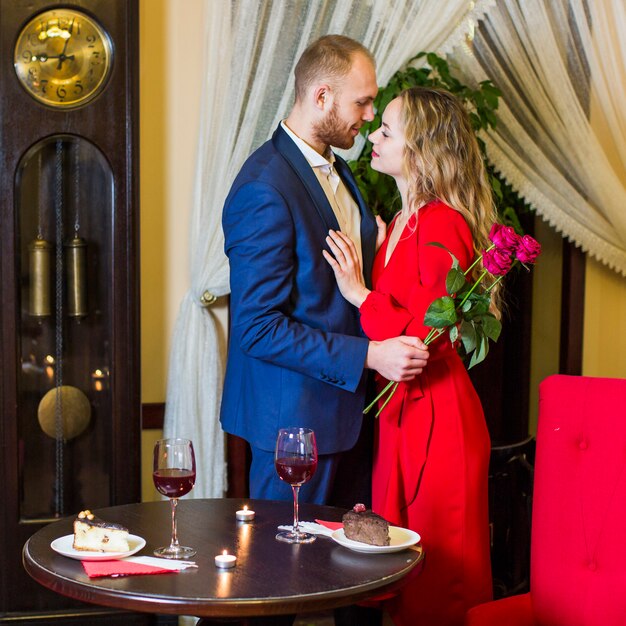 Uomo con le rose che abbracciano donna graziosa nel ristorante