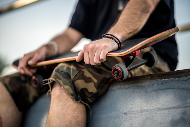 Uomo con maglietta nera e pantaloncini in possesso di uno skateboard nero sulle ginocchia