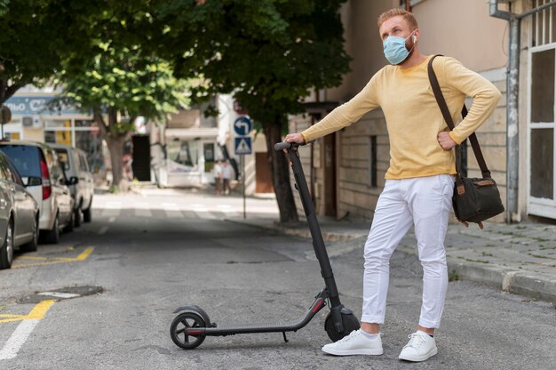 Uomo con mascherina medica che tiene il suo scooter
