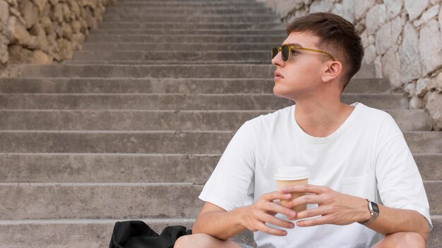 Uomo con occhiali da sole seduti sui gradini all'aperto e bere un caffè