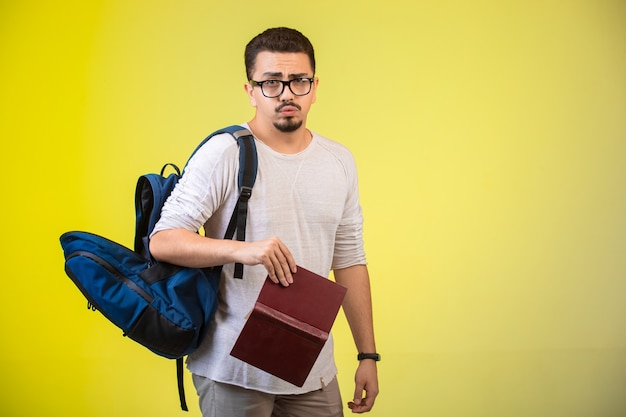 Uomo con occhiali, zaino e un libro.