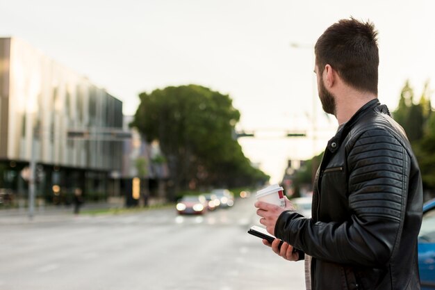 Uomo con smartphone e caffè attraversando la strada