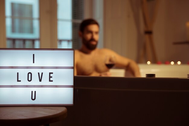 Uomo con un bicchiere di bevanda nella vasca idromassaggio e ti amo titolo sulla lampada