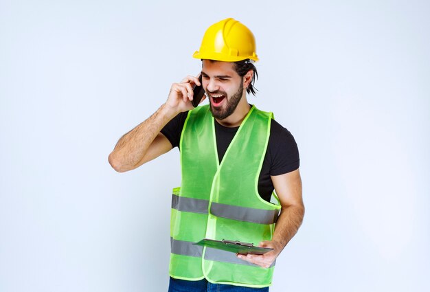 Uomo con un casco giallo e una cartella che urla al telefono.