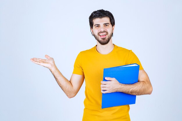 Uomo con una cartella blu che indica il suo collega sul lato sinistro e parla con emozioni.