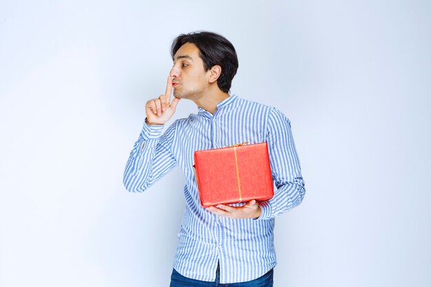Uomo con una confezione regalo rossa che chiede silenzio. Foto di alta qualità