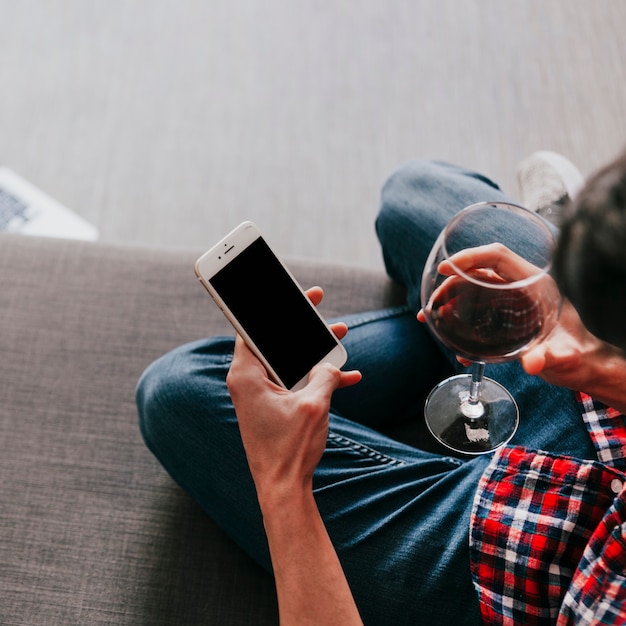 Uomo con vino e smartphone sul divano