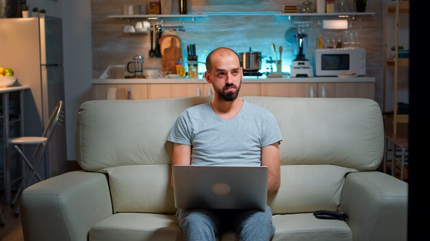 Uomo concentrato seduto sul divano e scrivendo un progetto online sul laptop
