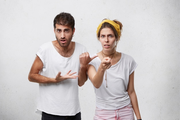 Uomo confuso con setole e acconciatura alla moda che punta il dito contro la donna che è in piedi vicino a lui cercando di renderla colpevole. Bella donna perplessa che guarda con insoddisfazione che ti punta