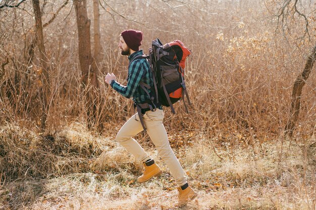 Uomo cool hipster che viaggia con lo zaino nella foresta autunnale con indosso una camicia a scacchi e un cappello