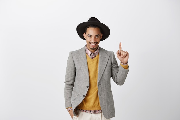 Uomo d'affari afroamericano bello impertinente in vestito che indica il dito verso l'alto, mostrando il numero uno